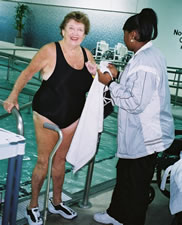 An older woman steps out of a pool with the help of her personal assistant.