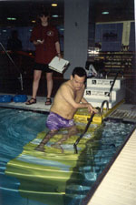 A man uses a transfer system, scooting down the steps, to enter the pool.