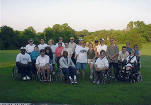 A large group of people on a golf course posing for a group photo. some are standing and others are seated in wheelchairs.
