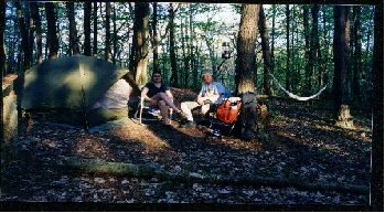Two people are sitting in front of a tent in the woods