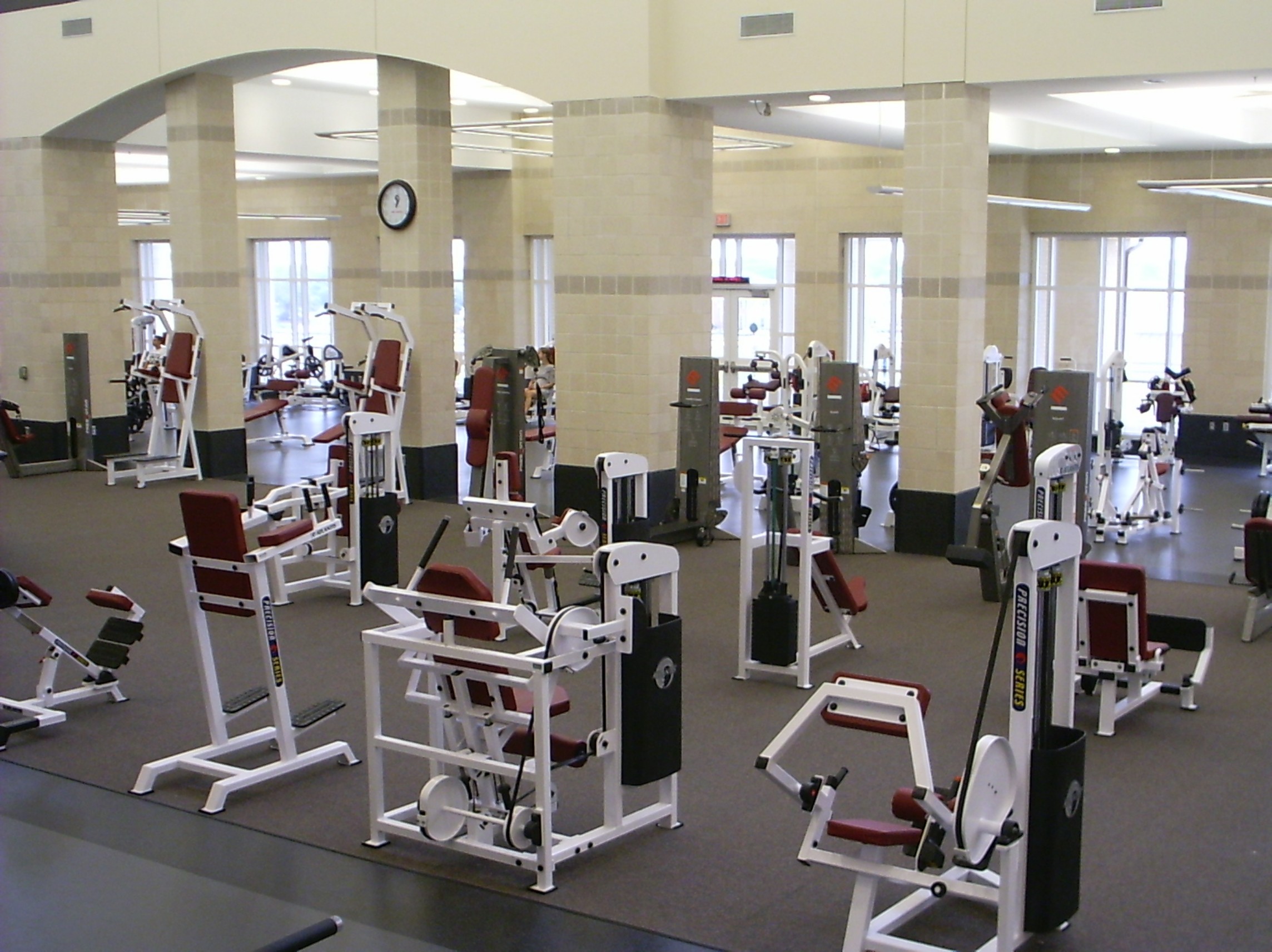 A fitness center with strength training equipment arranged in rows with significant space between each piece of equipment and each row.