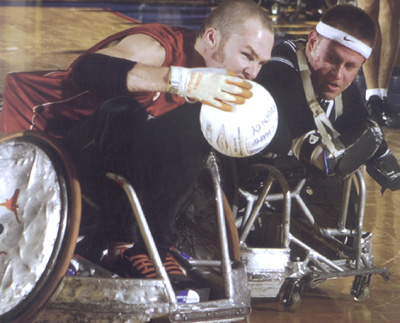 Two men in wheelchairs are engaged in an intense battle for the ball in a wheelchair rugby game.