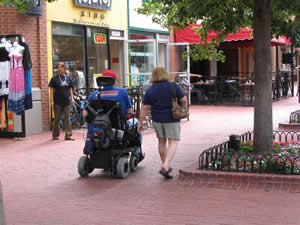 A woman walking with a man using a power wheelchair