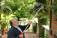 Man using long pruner to tend to flowers in overhead hanging basket