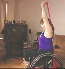 Woman who uses a wheelchair doing an overhead tricep extension with an elastic band.