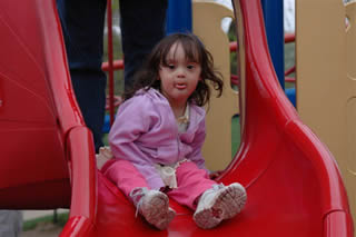 young girl with Downss syndrome slides down a slide at the park